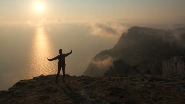 Silhuett av en ung kvinna armar utsträckta observation en vacker dramatisk solnedgång över ett hav från ett högt berg i Krim. — Stockvideo