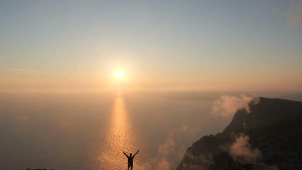 Silueta de una mujer joven brazos extendidos observando una hermosa puesta de sol dramática sobre un mar desde una alta montaña en Crimea . — Vídeos de Stock