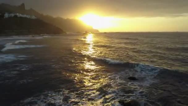 航空写真。海の波は、テネリフェ島、カナリア諸島のベニホビーチの近くに美しい夕日の光で岩にクラッシュし、スプレー. — ストック動画