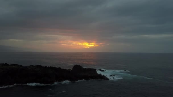 Voo lento acima do oceano tempestuoso em direção ao belo pôr-do-sol colorido. Drone aéreo de ondas oceânicas rolando sobre rochas negras . — Vídeo de Stock