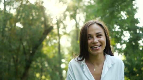 Primer plano retrato de chica femenina sonriente y alegre mirando a la cámara en otoño Parque. Atractiva jovencita está agitando su cabello, se vuelve hacia la cámara y se ríe. Belleza natural femenina en cámara lenta . — Vídeo de stock