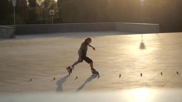 Joven patinador de pelo largo hombre está bailando entre conos por la noche en un parque de la ciudad al atardecer. Freestyle slalom Patinaje sobre ruedas entre conos . — Vídeos de Stock