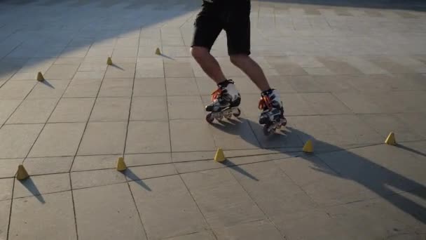 Primer plano de las piernas de un joven es patinar profesionalmente entre los conos en una bonita puesta de sol por la noche en un parque de la ciudad. Freestyle slalom Patinaje sobre ruedas entre conos . — Vídeos de Stock