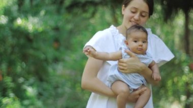 Bir parkta yeşil çimenlerin üzerinde yeni doğmuş kızıyla birlikte anne. Mutlu genç Anne ve Çocuk doğanın tadını çıkarıyor.