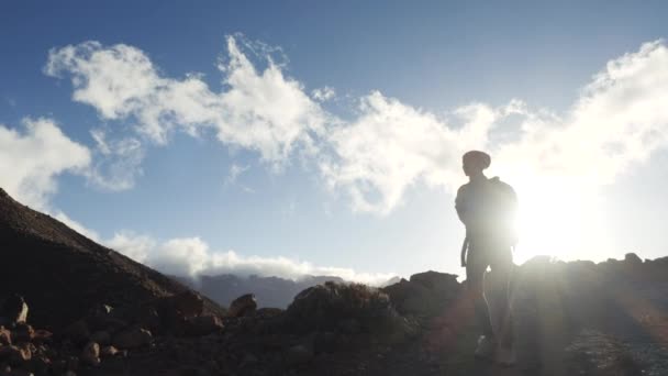 Sziluettje egy fiatal nő túró a hátizsákot gyaloglás felé csúcstalálkozó kék ég és a felhők. Lassított. Lady túrázás, gyönyörű hegyek a Kanári-szigeteken. — Stock videók