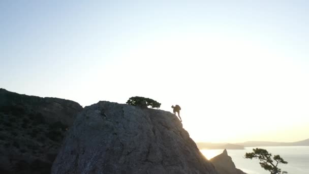 Luftaufnahme einer jungen Frau, die bei Sonnenaufgang auf der Krim einen Berg gegen das Meer klettert. Dame hebt die Hände auf dem Berggipfel in wunderschöner Landschaft. — Stockvideo