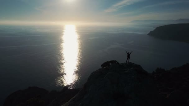 일출에 바다에 대한 산의 꼭대기에 서 젊은 여성의 공중 실루엣. 팔을 뻗은 크림 반도의 산 꼭대기에 있는 행복한 청녀. 정상에 있는 레이디 등산가 — 비디오