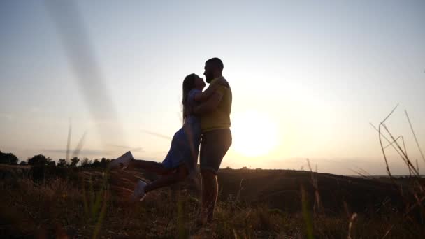 Uma história de amor de um jovem casal encantador na paisagem rural ao pôr-do-sol. Silhueta de barbudo jovem segurando e girando sua namorada em deslumbrante pôr do sol dourado . — Vídeo de Stock