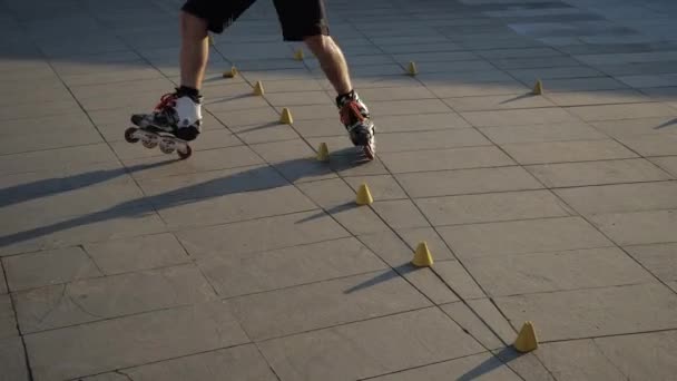 Close-up benen van een jonge man is professioneel schaatsen tussen kegels op een mooie avond zonsondergang in een stadspark. Freestyle slalom roller skating tussen kegels. — Stockvideo