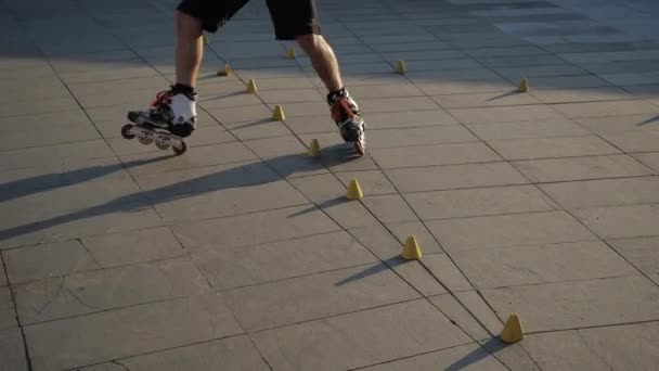 Nahaufnahme Beine eines jungen Mannes ist professionell Schlittschuhlaufen zwischen Zapfen an einem schönen Abend Sonnenuntergang in einem Stadtpark. Freestyle Slalom Rollschuhlaufen zwischen Kegeln. — Stockvideo