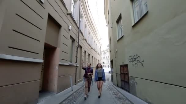 Dos jóvenes caminando por las estrechas calles del casco antiguo de Vilna mientras hablan y ríen . — Vídeos de Stock