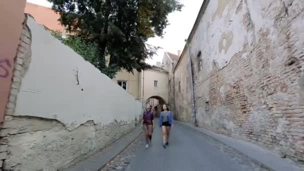 話しながら笑いながらビリニュス旧市街の狭い通りを歩く二人の若い女性. — ストック動画