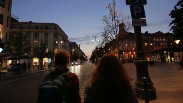 Dwie młode kobiety chodzą w nocy miasta wileńskiego Starego miasta. Spacer wśród pięknych świateł nocnych Europy i życia europejskiego miasta w nocy. Obrót kamery. — Wideo stockowe