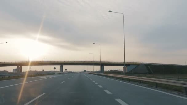 POV jazdy wzdłuż szerokiej pustej drogi porannej wcześnie rano podczas wschodu słońca.. Punkt widzenia jazdy, widok z wnętrza samochodu na autostradę w Polsce. — Wideo stockowe