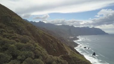 Güzel tropikal manzara, kıyı şeridi, orman ve dramatik bulutlar ile kaplı dağlar kuşlar göz görünümü. Tenerife'de Atlantik Okyanusu üzerinde toprak bir dağ yolunda bir arabanın havadan görünümü.