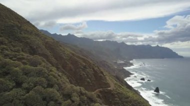Güzel tropikal manzara, kıyı şeridi, orman ve dramatik bulutlar ile kaplı dağlar kuşlar göz görünümü. Tenerife'de Atlantik Okyanusu üzerinde toprak bir dağ yolunda bir arabanın havadan görünümü.