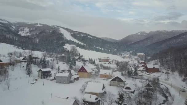 Vista aérea de un coche que se mueve en la carretera de invierno en el pueblo de los Cárpatos a la estación de esquí Pilipets. Vista de aves de casas cubiertas de nieve. Paisaje rural en invierno . — Vídeo de stock