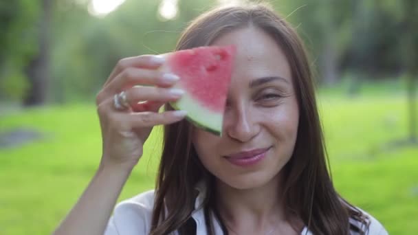 Närbild porträtt av flickan luktar arom och äta en röd hälsosam saftig vattenmelon, lurar och skrattar på en grön bakgrund. Frukt-fördelarna med gröna livsmedel och naturlig hälsosam kost. — Stockvideo