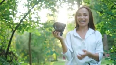 Güzel gülümseyen ve beyaz gömlek giyen gülen kız fotoğrafçı yeşil yaprakları yumuşak bir arka plan üzerinde bir parkta fotoğraf yapıyor. Bir kadın gün batımında güneş ışınları ile doğa fotoğrafları.