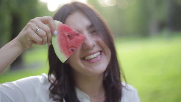 Closeup portré lány szagú illat és az evés egy piros egészséges lédús görögdinnye, bolondozás és nevetve a zöld háttér. Gyümölcsök-a zöld ételek és a természetes egészséges táplálkozás előnyei. — Stock videók