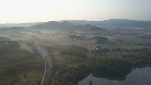 Filmszerű légifelvételek egy vasútállomás melletti hegyekben, egy tónál. Ködös napkelte in Mountains. — Stock videók