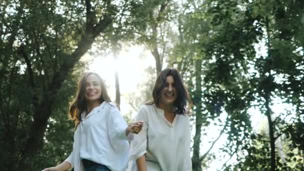 Dos chicas morenas jóvenes felices riendo y bailando en cámara lenta. Feliz impresionante Las mujeres con el pelo soplando en el viento mirando a la cámara, saltando y sonriendo . — Vídeo de stock