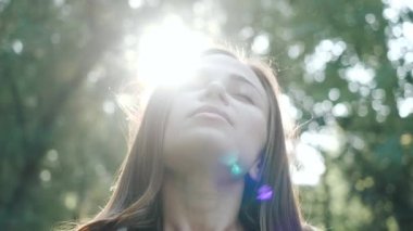 Gülümseyen, neşeli, ipek saçlı, rüzgarda savrulan kadın portresi kameraya bakar, gözlerini kapatır ve taze rüzgardan zevk alır. Ağır çekimde kadın doğal güzelliği.