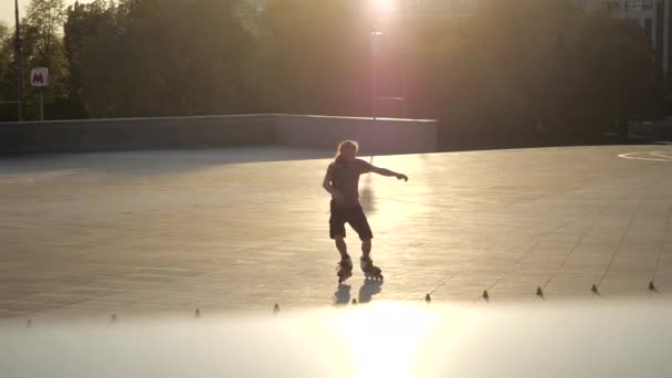 Der junge, langhaarige, bärtige Rollschuhfahrer tanzt abends bei Sonnenuntergang im Stadtpark zwischen Zapfen. Freestyle Slalom Rollschuhlaufen zwischen Kegeln. — Stockvideo