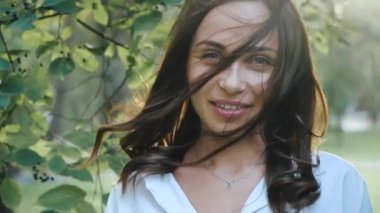 Gülümseyen, neşeli, ipek saçlı, rüzgarda savrulan kadın portresi kameraya bakar, gözlerini kapatır ve taze rüzgardan zevk alır. Ağır çekimde kadın doğal güzelliği.