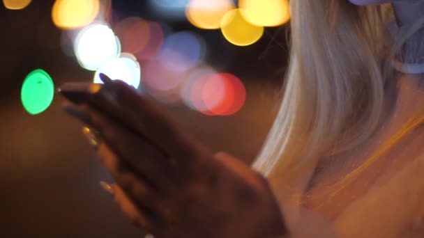 Primo piano di mani di donna bionda con smartphone in città di notte. Digitando il messaggio sullo smartphone nella strada della città di notte. Ragazza sms su smartphone . — Video Stock