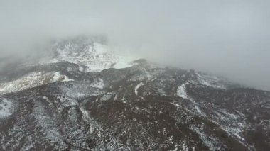 Şiddetli çöl dağ manzarası. Hayatta kalmak için zor koşullar. Tenerife 'deki Teide volkanının kar ve bulutlarla kaplı zirvesinin havadan görüntüsü..