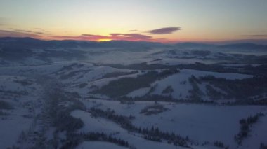 Kışın gün doğumunda Karpat Dağları 'nın üzerinden uçacağız. Kışın yüksek bir yerden kırsal alan. Karla kaplı bir dağ köyünün havadan görünüşü.