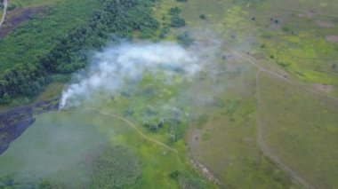 Yanan yeşil alanda dumanın içinden uçmak, doğa manzarasında vahşi ateş, İHA 'dan gelen hava görüntüleri. Hava manzarası, yanan çimlerin üzerinde uçmak, bir ormanın yanında.