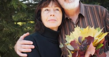 Mutlu yaşlı çift, sonbaharda bir çam ağacının altında kucaklaşmayı sever. Yavaş çekimde..