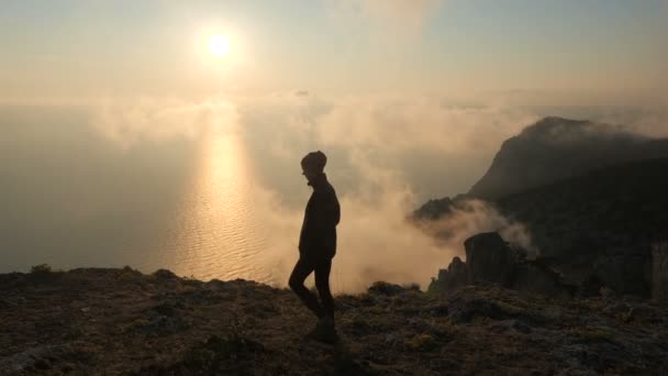 Η Silhuette of Young Woman περπατά κατά μήκος ενός βράχου πάνω από μια θάλασσα και παρατηρεί ένα όμορφο δραματικό ηλιοβασίλεμα από ένα ψηλό βουνό στην Κριμαία. — Αρχείο Βίντεο