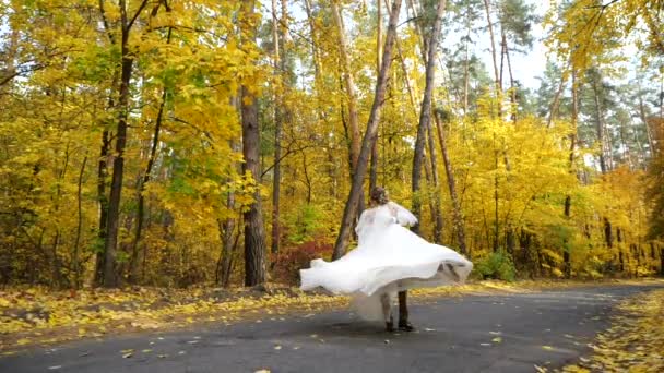 En cámara lenta. Novio gira novia alrededor en el bosque de otoño mientras baila en cámara lenta entre los árboles de otoño de colores. Joven atractivo Feliz amor recién casados bailan y giran en un parque . — Vídeo de stock