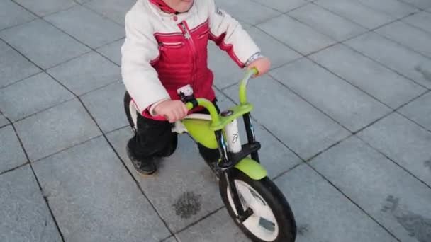 Kleine lachende vrolijke jongen rijdt op een groene fiets in een stadspark, close-up. Kleine motorrijders met helmen in een stadspark. — Stockvideo