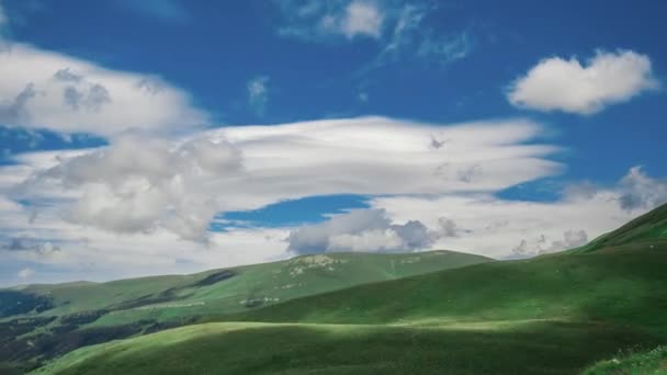 山の美しい広い丘の上からの眺めは、澄んだ空と谷と水平線の背景に大きな雲の層の下の草で覆われています。自然界の空中ショットタイムラプス. — ストック動画