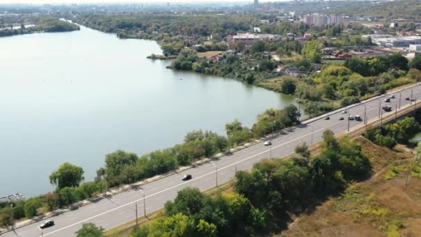 Vista aérea del tráfico por carretera que pasa por el puente sobre el río sobre un fondo de árboles y casas en el caluroso día soleado de primavera en la ciudad de Jarkov, Ucrania. Vista superior de los coches que conducen en puente en verano . — Vídeo de stock