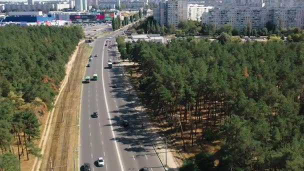 우크라이나 하리코프의 어느 무더운 여름날, 소나무 숲 과 자동차들 사이를 지나는 아스팔트 도로 위를 날면서, 우크라 이나 하르 코프에 있는 주거용 건물들의 배경을 달리고 있다. 도로 교통, 맨 위 뷰. — 비디오