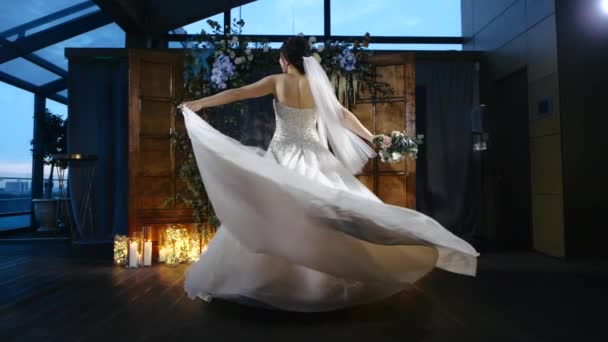 Вид спереди на красивую и очаровательную европейскую невесту в элегантном свадебном платье и букеты цветов в руках, закручивающуюся перед алтарем и исполняющую традиционный танец для гостей вечером — стоковое видео
