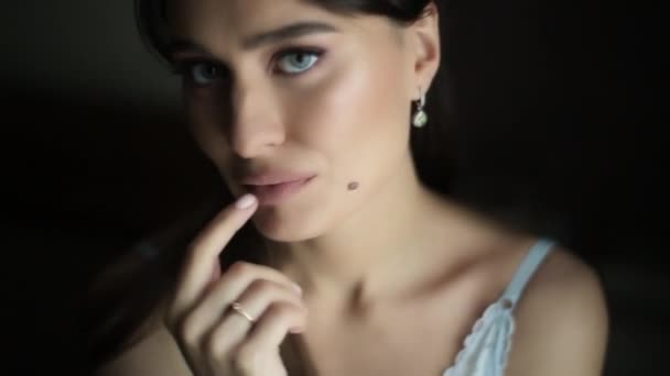 Una hermosa dama sexy en un elegante desprecio mira a la cámara, sonríe y pasa su mano sobre sus labios. Modelo con maquillaje, morena de ojos azules de pelo largo, retrato con lunar . — Vídeo de stock