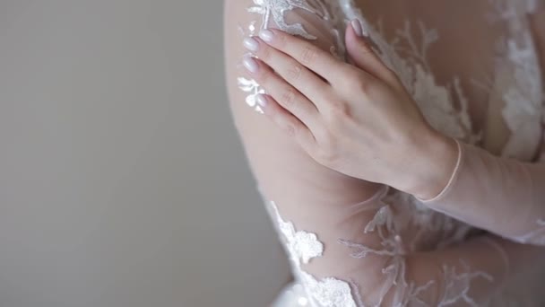 Una giovane bella sposa europea in un abito da sposa in pizzo corre la mano con una manicure sulla spalla, si abbraccia, il modello posa in una stanza luminosa, grande piano . — Video Stock