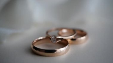 Üç güzel altın yüzük, bir elmas nişan yüzüğü ve beyaz bir masanın üzerinde hafif kumaş arka planda duran bir nişan yüzüğü. Hediyeler ve romantizm, dekor. Gelin ve damadın şenlikli atmosferi.