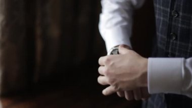 Şık bir adam pahalı saatini eline göre ayarlar. Gümüş saati sıkılaştıran erkek ellerinin yakın çekimi. Beyaz gömlekli ve ekose yelekli zengin damat sabah odasında kol saati takıyor..