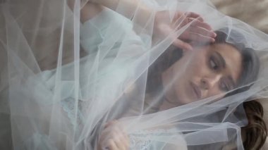 Sabahları güzel ve seksi bir gelinin duvağın altında turkuaz dantelli yatakta yatarken yakın plan çekimi. Muhteşem esmer gelin kendini pahalı bir otelin yatak odasında peçeyle örttü..