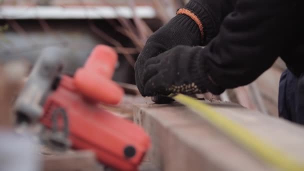 Primo piano del lavoratore non identificato con i guanti da lavoro che misura la lunghezza e la larghezza della tavola con il metro a nastro per la lavorazione e la segatura con una circolare. Costruzione di case telaio. Riparazione con smerigliatrice . — Video Stock