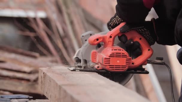 Close-up in slow motion van een mannelijke timmerman in handschoenen die een dik bord zagen met een cirkelvormige achtergrond op wazige stokken. Ik zag een boom met een molen. Zaagsel in de lucht. Frame woningbouw. — Stockvideo