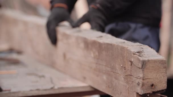 Widok z bliska na niezidentyfikowanego pracownika w rękawiczkach roboczych obracającego grubą tarczę pilarską ze szlifierką. Człowiek patrzy na kawałek drewna i myśli, jak pokroić go na okrągło. Naprawa konstrukcji obudowy ramy. — Wideo stockowe