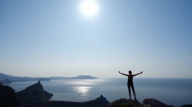 Sportif kız Ukrayna 'nın Kırım kentindeki güneş ve Karadeniz manzarasına hayran. Yürüyüş. Genç bayan turist dağın tepesinden güzel manzarayı düşünür, ellerini kaldırır ve uzar..